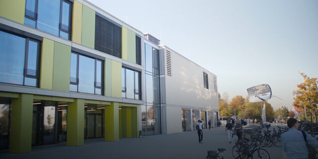 Bild – Aussenansicht einer modernen Schule mit großen Fenstern und farbigen Fassadenbausteinen