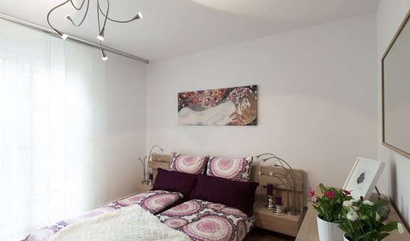 Innenansicht Schlafzimmer; Bett und Nachtschrank, über dem Bett hängt ein Gemälde