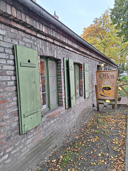Exterior view of the Lehmsofa café. A wooden sign with an illustrated steaming coffee cup invites you to enter. 