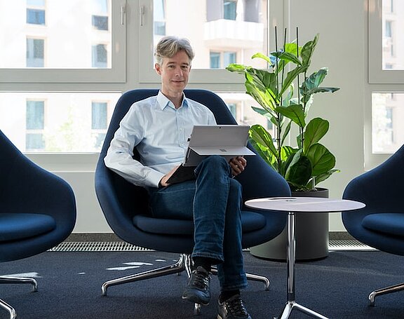 Mann mit grauem Haar sitzt mit Laptop auf einem Stuhl
