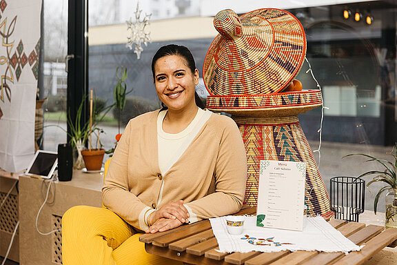Ein Foto von Blen Baheru, die am Tisch ihres Cafés sitzt und in die Kamera lächelt