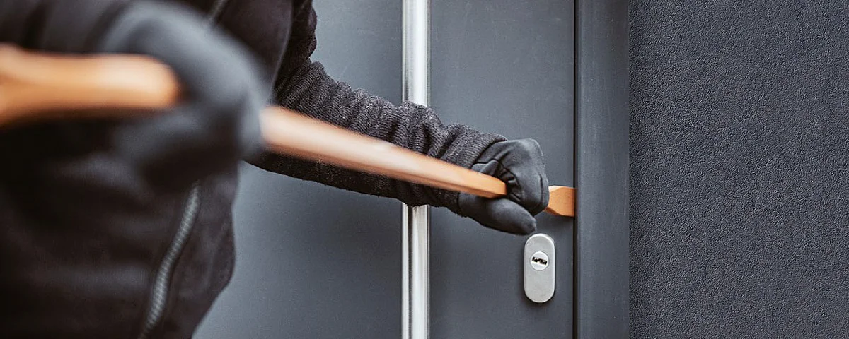 Eine vermummte Person versucht mit einem Brecheisen, eine Haustür aufzubrechen.