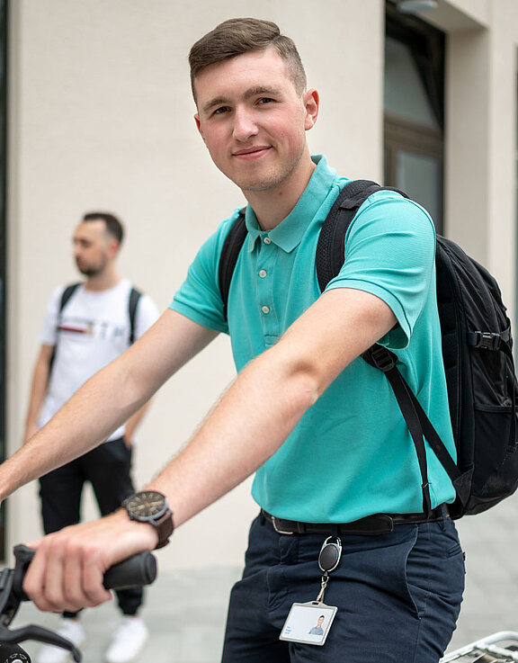 Junger Student im grünen T-Shirt sitzt auf dem Fahrrad und lächelt in die Kamera