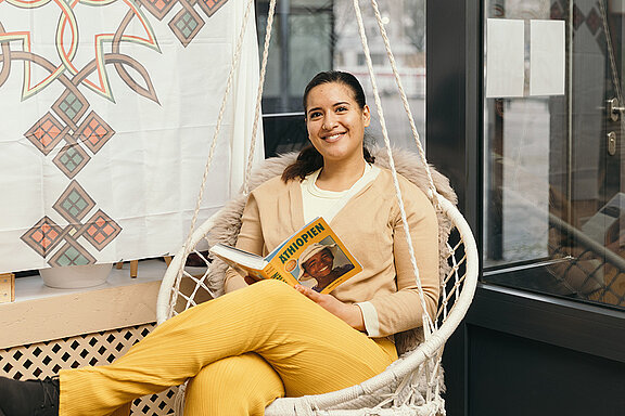 Ein Foto von Blen Baheru, die im Sessel sitzt, in die Kamera lächelt und ein Buch über Äthiopien in ihren Händen hält