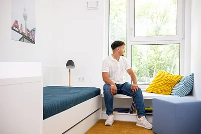 Ein Mann sitzt in einem Schlafzimmer neben dem Bett.