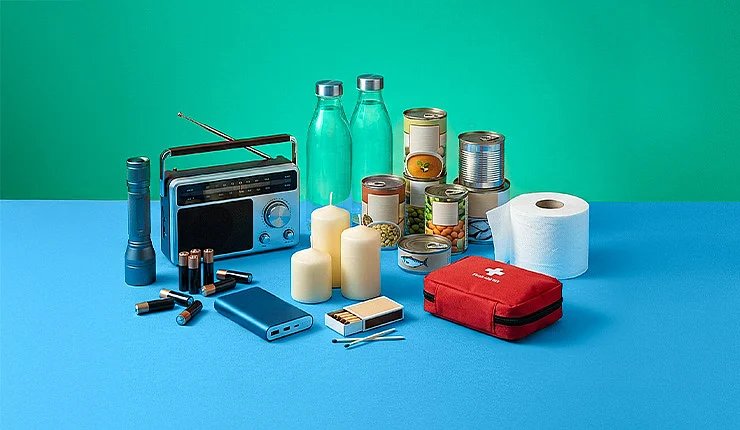 Ein Foto mit Basis-Notfallprodukten wie Kerzen, Wasserflaschen, Erste-Hilfe-Set, Konserven usw.