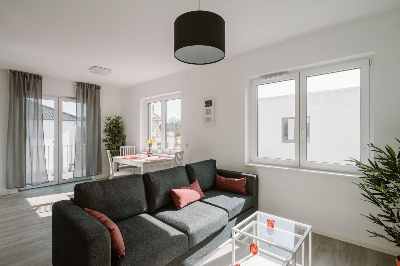Bild – Wohnzimmer mit schwarzer Stoff-Couch und kleinem Esstisch