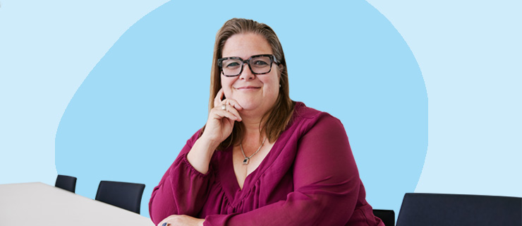 Frau Seuring sitzt an einem Tisch und legt ihren Kopf in ihre rechte Hand. Dabei schaut sie zur Kamera.