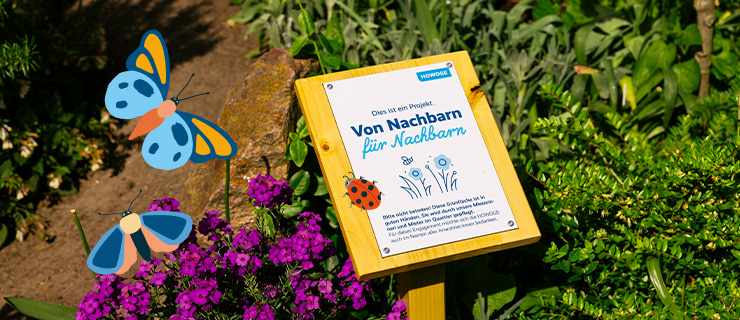 Eine Infotafel vor einem Blumenbeet. Auf der Tafel steht "Von Nachbarn für Nachbarn".