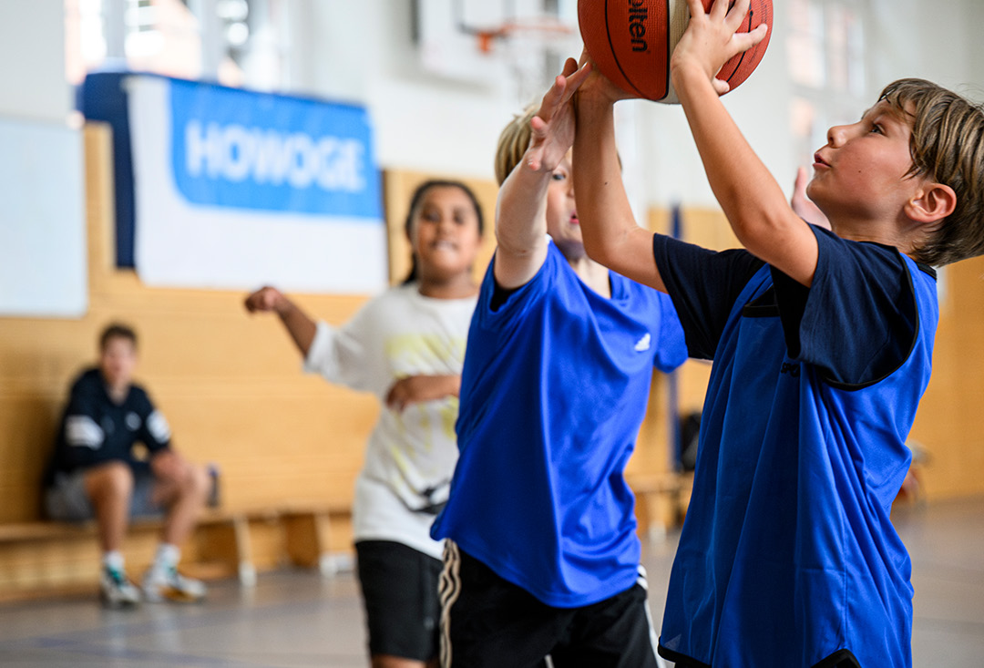 3 Kinder spielen Basketball; im Hintergrund ein Banner der HOWOGE