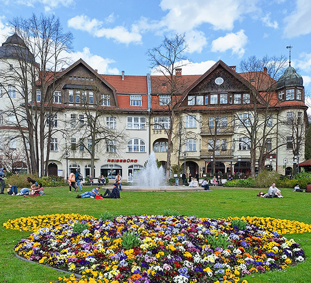 Mexikoplatz – a meadow with colorful flowerbeds where people sit. Behind it, houses. 