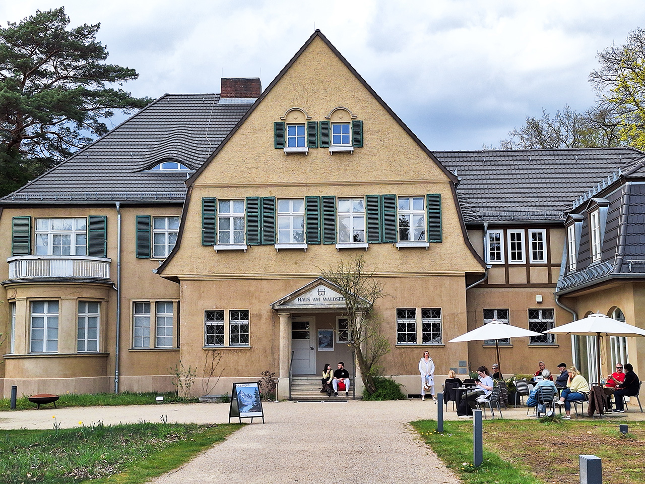 An older house with shutters. Above the entrance, the sign "Haus am Waldsee" (House by the Forest Lake) is written on the wall.