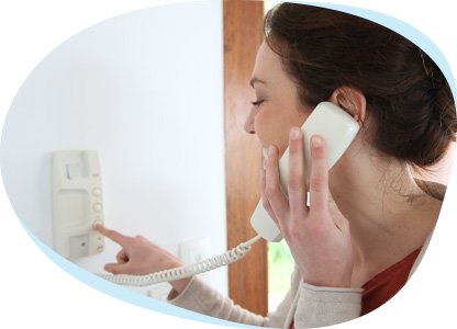 Eine Frau spricht durch eine Türsprechanlage. Sie hält dafür einen Hörer in der Hand. 