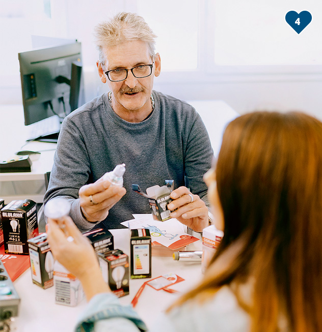 eine Person an einem Schreibtisch, der einer Person etwas erklärt