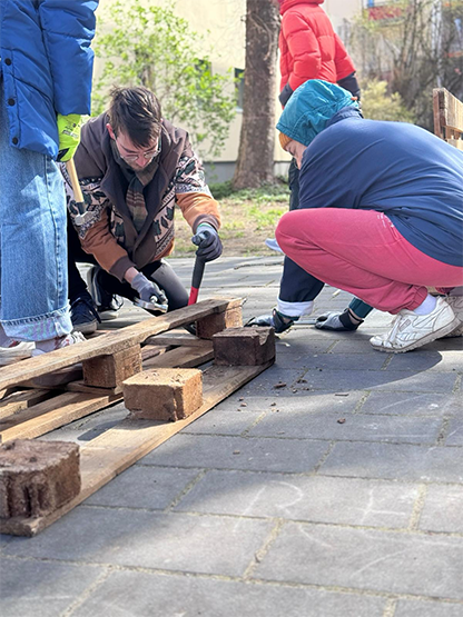 Mehrere Personen arbeiten im Freien gemeinsam an Holzpaletten. Sie setzen ein handwerkliches Projekt um, möglicherweise im Rahmen einer Gemeinschaftsaktion.